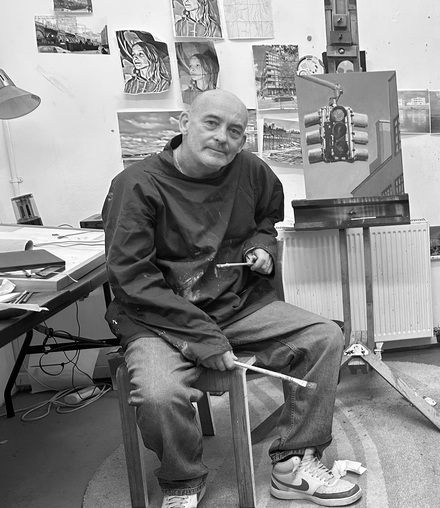 Artist sitting in a studio with art supplies and paintings on the walls.
